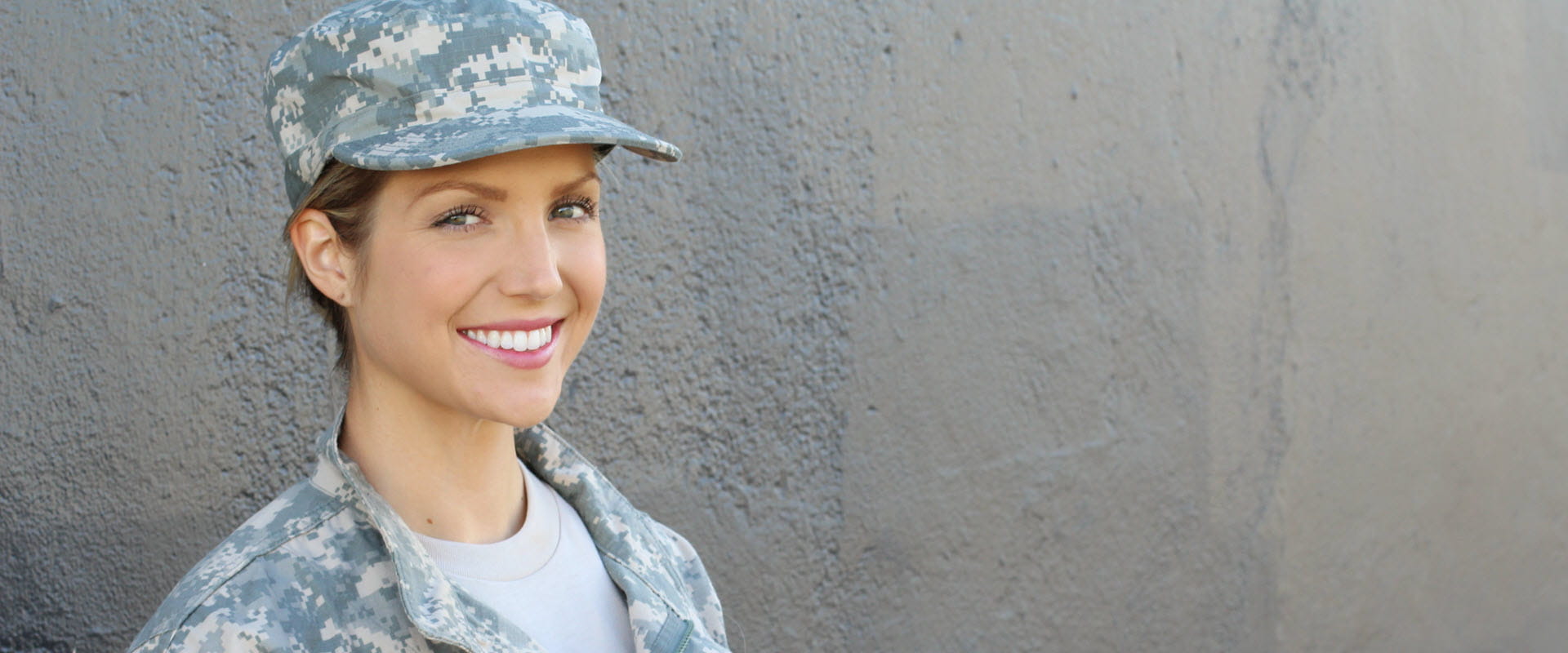 Person in military uniform smiling while standing against a textured wall. Person in military uniform smiling while standing against a textured wall.