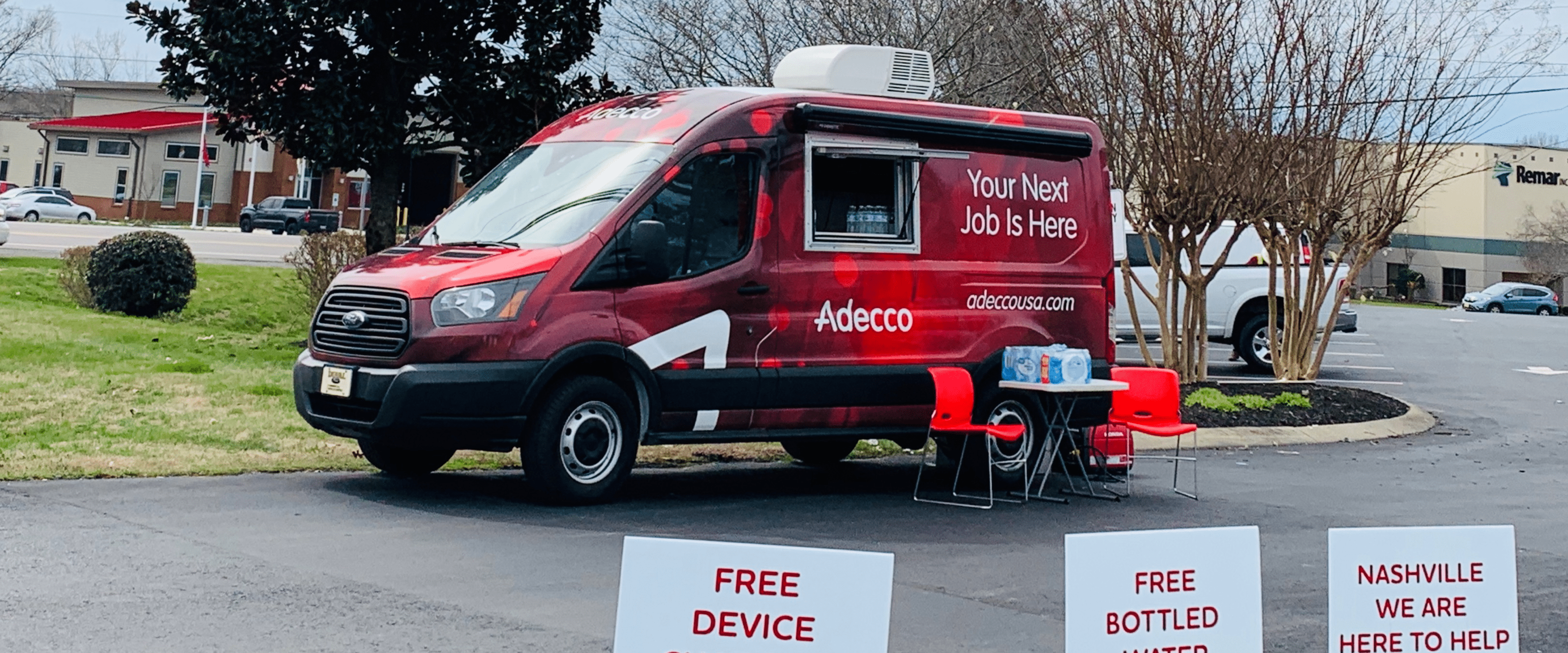 A red van with Adecco logos sits in a driveway. There are chairs sitting out front and a small table. A red van with Adecco logos sits in a driveway. There are chairs sitting out front and a small table.