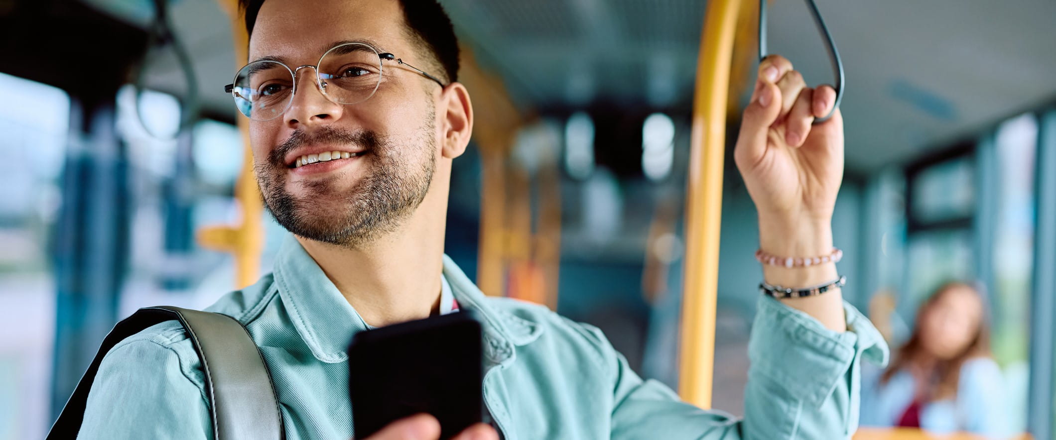 A person stands on a bus holding the support pole and their phone in the other hand A person stands on a bus holding the support pole and their phone in the other hand