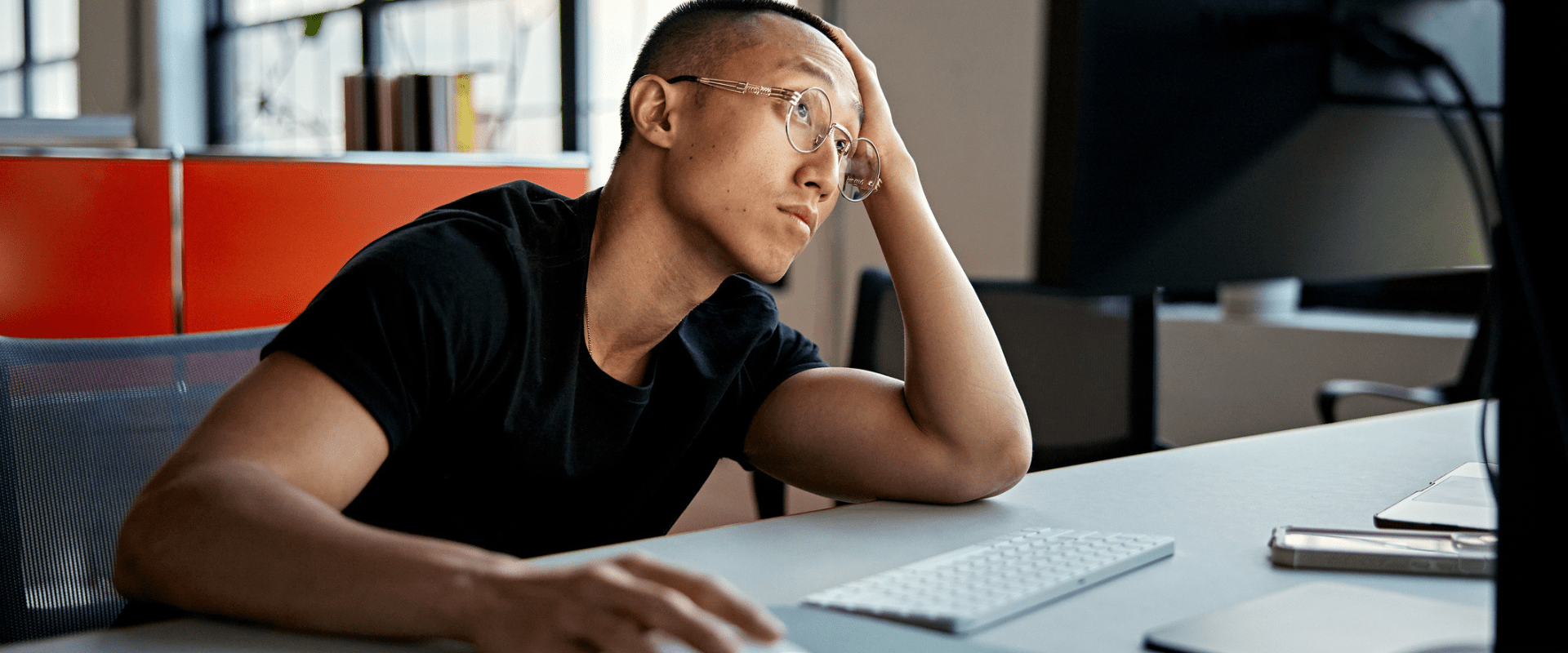 A young worker sits at a computer, looking frustrated