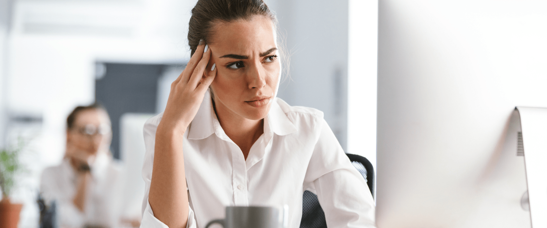 A frustrated worker looks at their desktop computer in an open office.