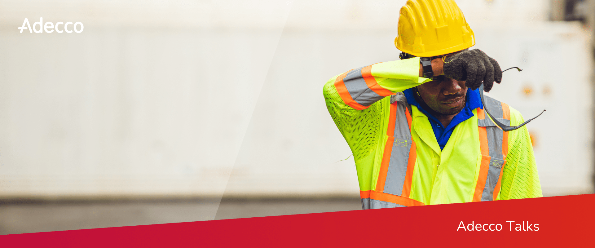 A worker wearing a safety vest and hard hat wipes sweat from their forehead. A worker wearing a safety vest and hard hat wipes sweat from their forehead.