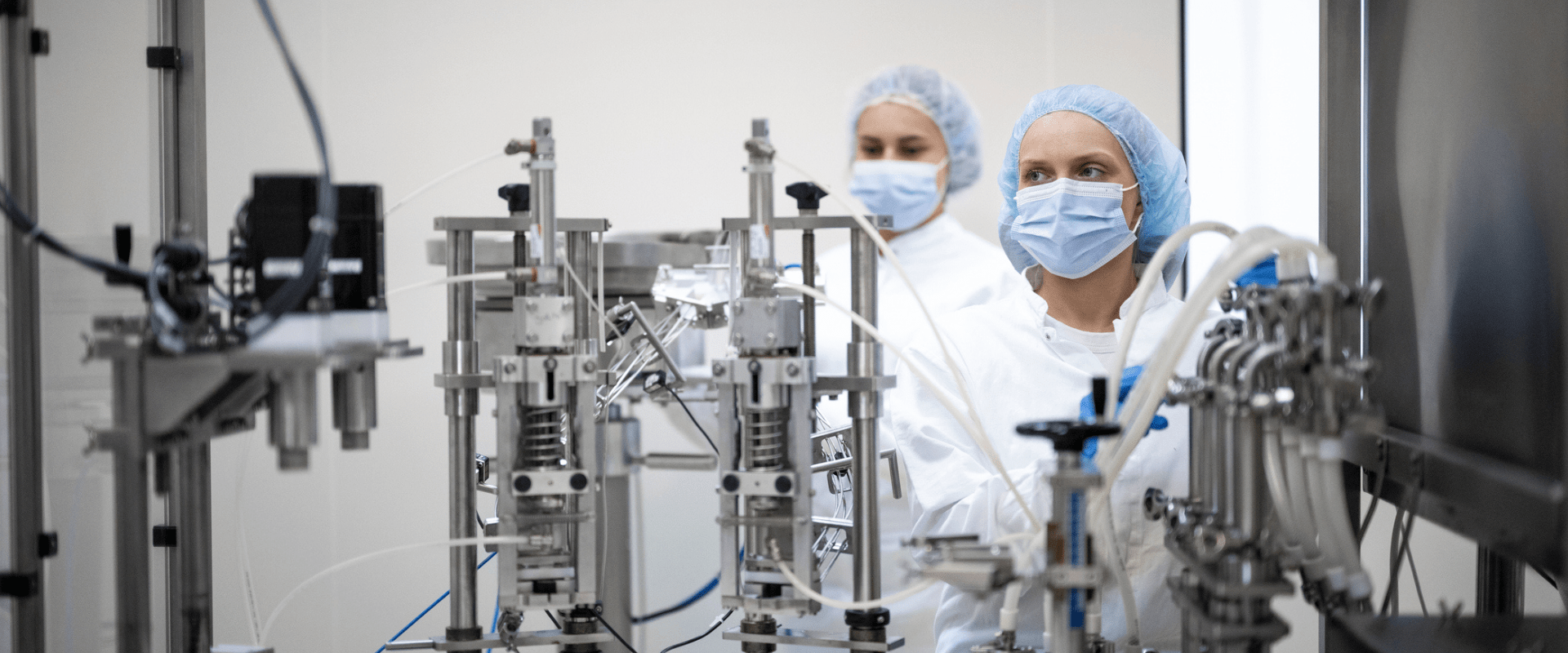 Two people in protective gear work at a biomanufacturing plant. 