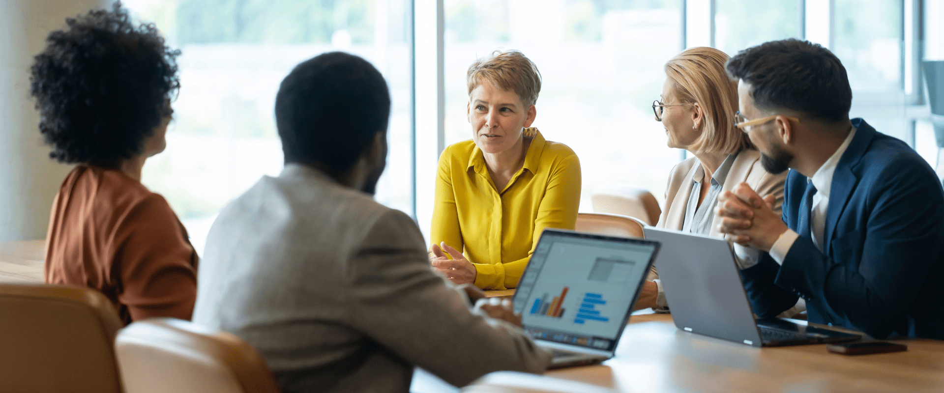 A group of people sit at a conference room table, looking at one person who is speaking.