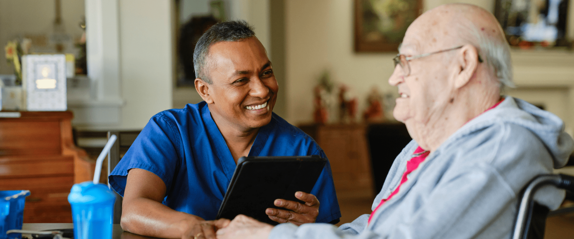 A nurse sits at a table with a person in a wheelchair at a care facility. A nurse sits at a table with a person in a wheelchair at a care facility.