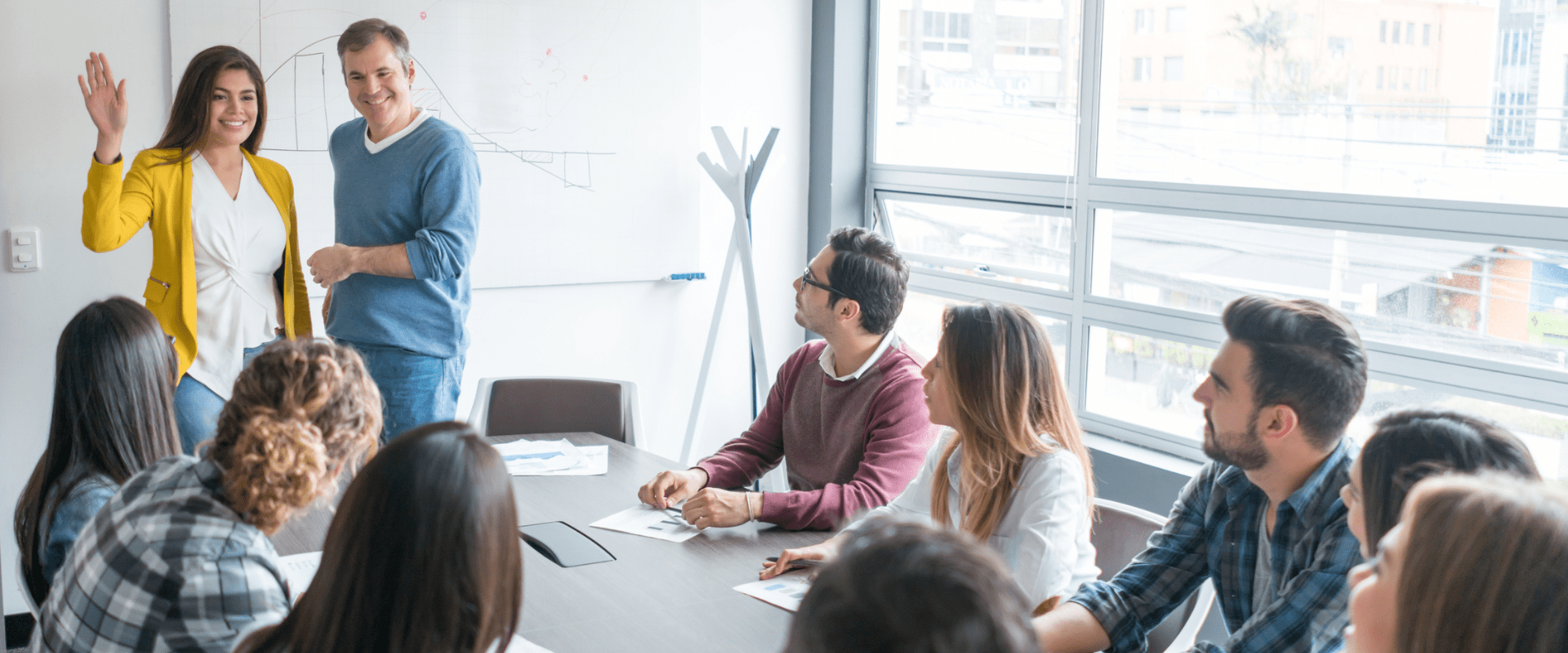 A manager introduces a new worker to a full conference room A manager introduces a new worker to a full conference room