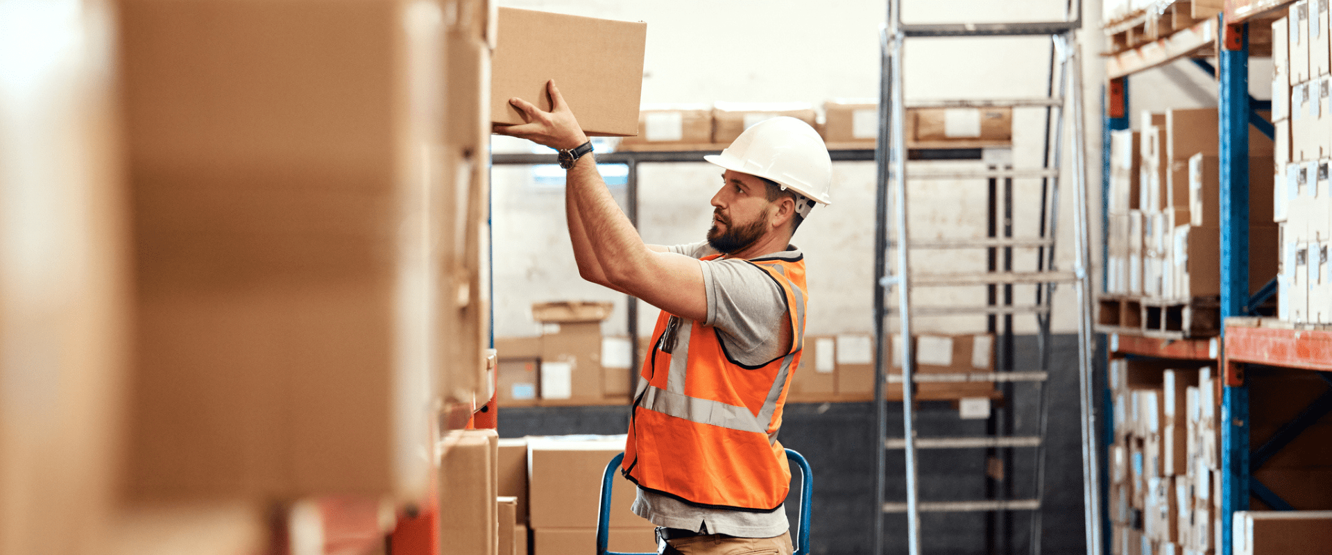 A worker in a warehouse places a box on a high shelf A worker in a warehouse places a box on a high shelf