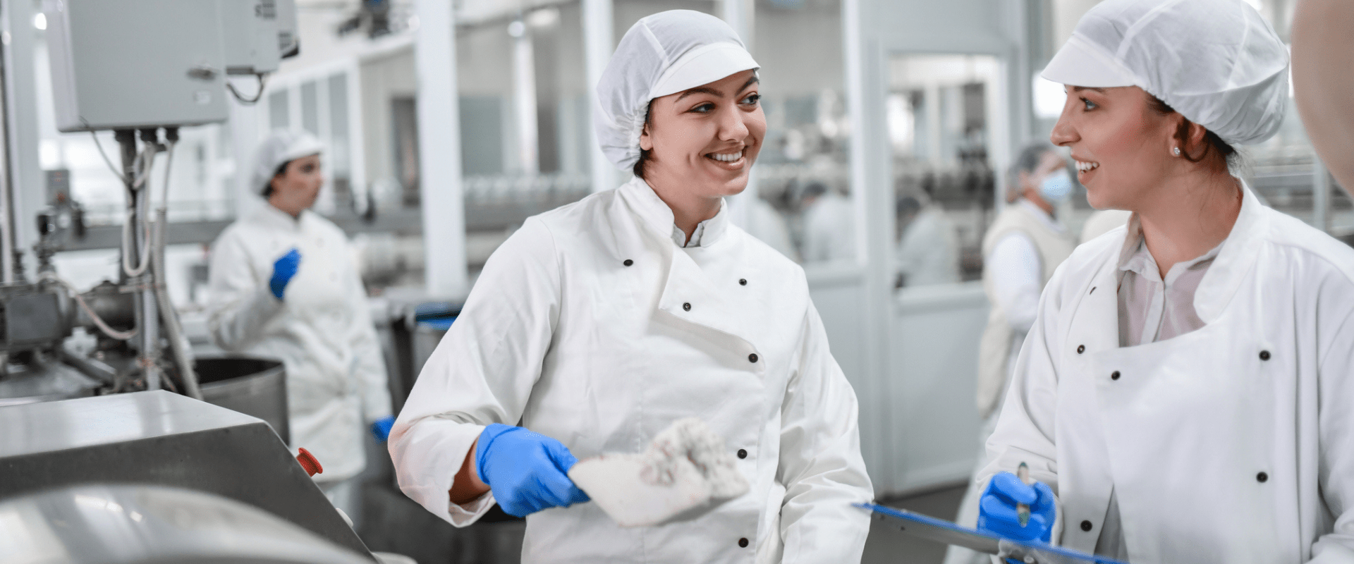 Two workers in a food processing plant are wearing hygienic clothing and hair coverings. They are laughing and talking. Two workers in a food processing plant are wearing hygienic clothing and hair coverings. They are laughing and talking.
