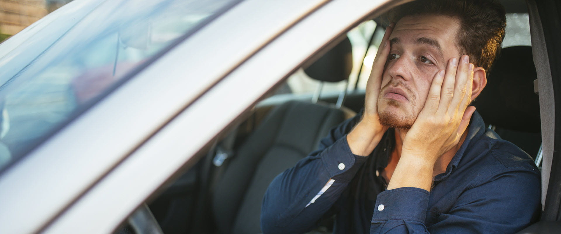 An individual sits in their car, with their hands on their face, seeming overwhelmed. An individual sits in their car, with their hands on their face, seeming overwhelmed.
