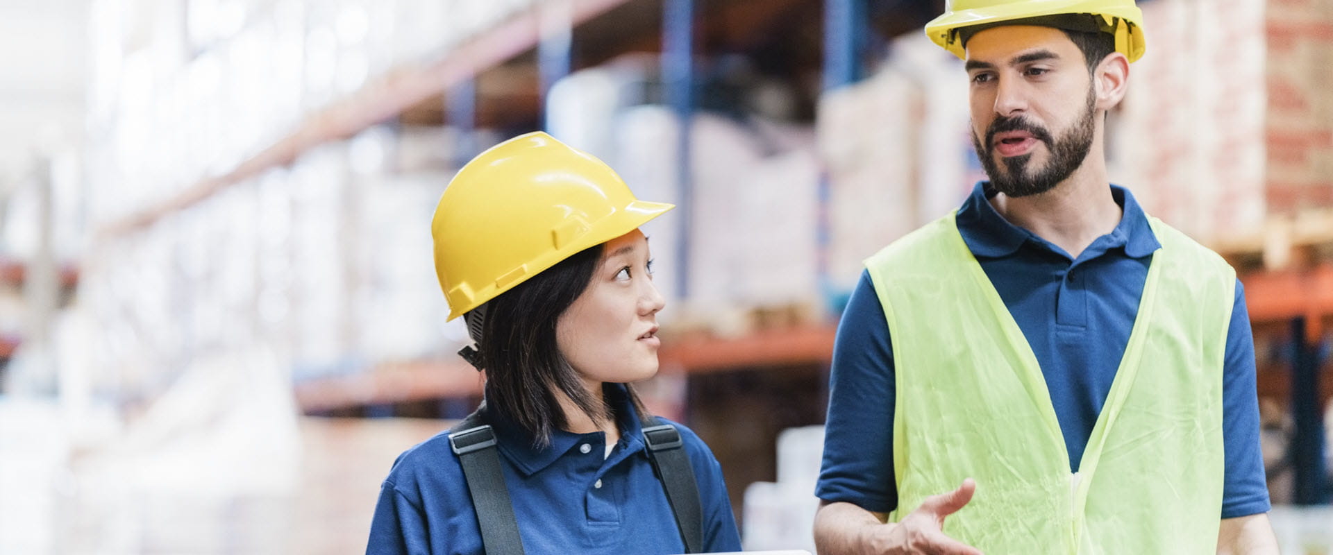 Two workers in hardhats talk, while walking in a warehouse Two workers in hardhats talk, while walking in a warehouse