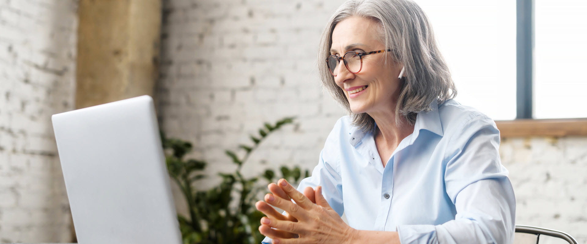 A gray-haired individual smiles while looking at a laptop. A gray-haired individual smiles while looking at a laptop.