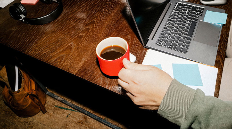 Person working on laptop with coffee on desk Person working on laptop with coffee on desk