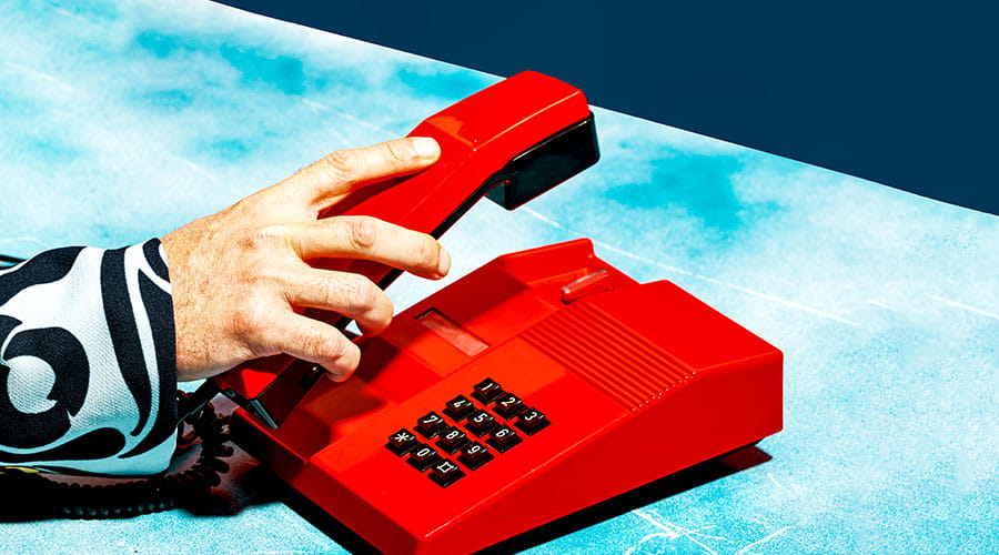 Mano che tiene la cornetta rossa del telefono sulla scrivania