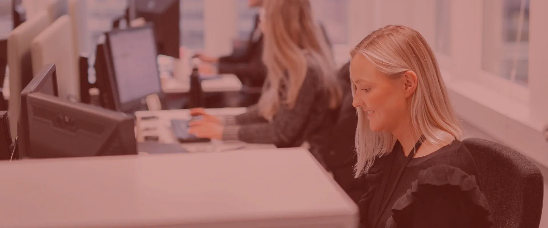 Kvinne sitter i kontorlandskap og smiler ned mot arbeidet sitt. Kvinne sitter i kontorlandskap og smiler ned mot arbeidet sitt.